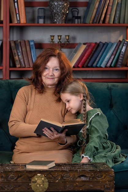 Happy grandma and granddaughter reading book together and having fun at home