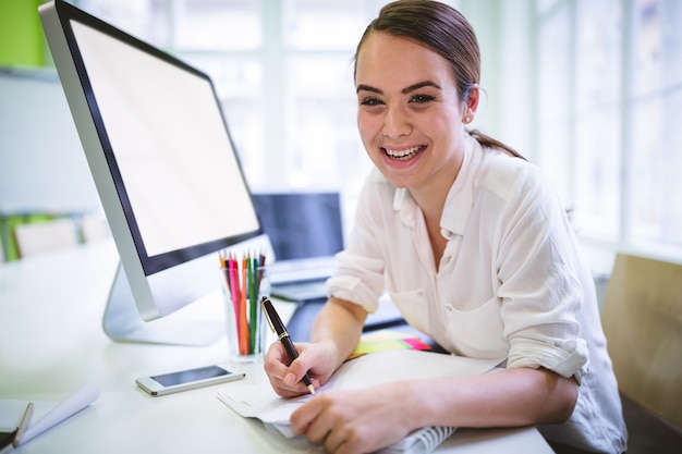 Happy graphic designer writing on book at desk