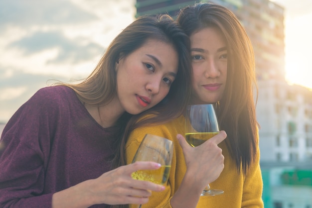 Il gruppo felice di ragazze asiatiche gode della risata e del bicchiere di vino spumante allegro alla festa sul tetto