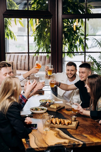 Foto felice gruppo di amici che bevono e tintinnano con birra e cocktail al ristorante bar birreria concetto di stile di vita delle bevande con ragazzi e ragazze che si divertono insieme