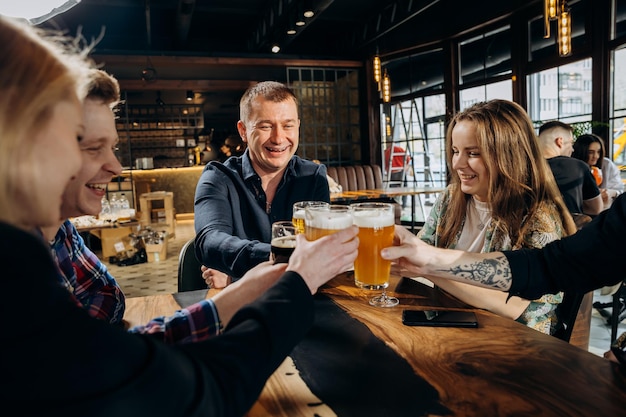 ビール醸造所のバーレストランでビールやカクテルを飲み、チリンチリンと鳴らす友人の幸せなグループ