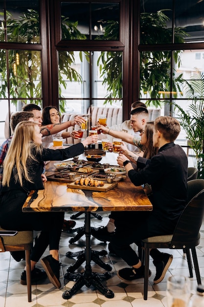Foto gruppo felice di amici che bevono e tintinnano con birra e cocktail al ristorante bar birreria