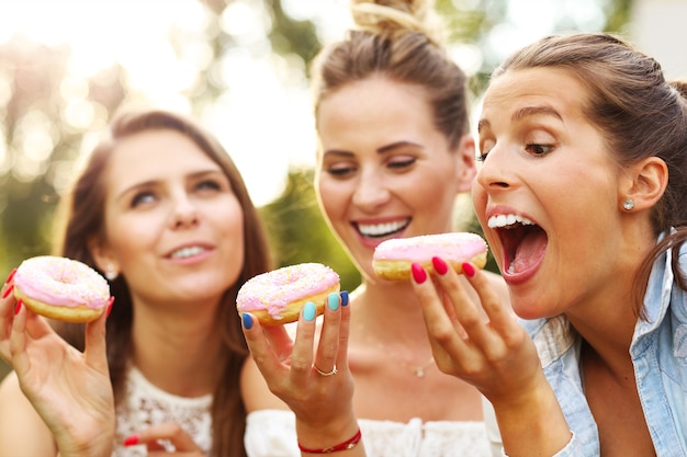 happy group of friends eating donuts outdoors