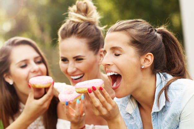 happy group of friends eating donuts outdoors