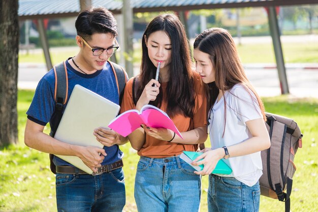 大学に立っている幸せなグループの友達の学生が一緒にノートブックを読む