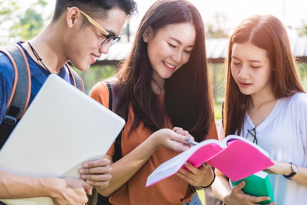 大学に立っている幸せなグループの友達の学生が一緒にノートブックを読む