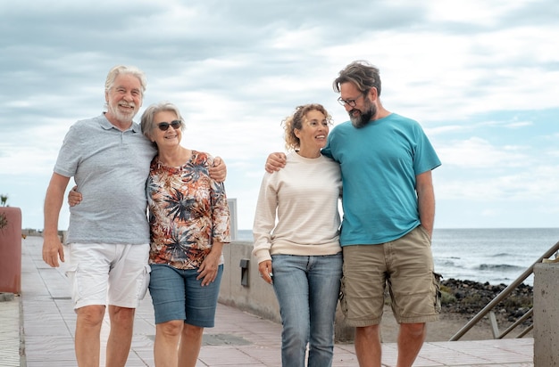 Счастливая группа семьи из нескольких поколений остается вместе, гуляя по пляжу, четыре улыбающихся человека