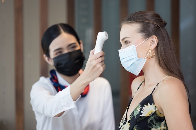 Ospite felice che controlla la febbre con il termometro digitale per la scansione e la protezione dal coronavirus covid-19 alla reception dell'hotel