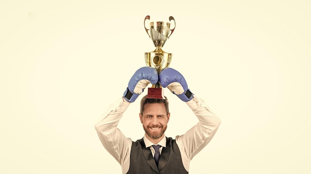 Happy guy in boxing gloves and formalwear hold champion cup isolated on white background victory