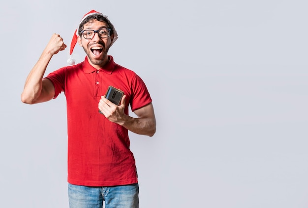 Happy guy in christmas hat holding cellphone celebrating People with santa hat celebrating a promotion with the cell phone Happy smiling man in christmas hat holding cellphone celebrating