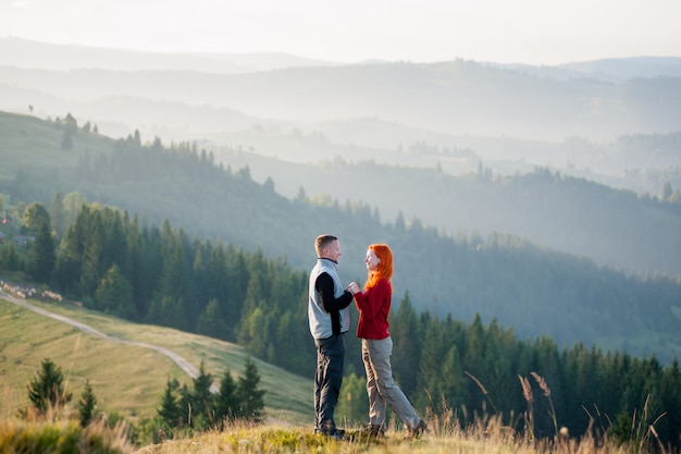 Happy guy and girl standing facing each other on a hill at the mountains in the morning