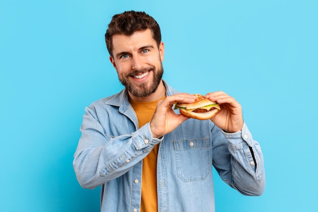 happy guy holding burger eating junk food over blue backdrop