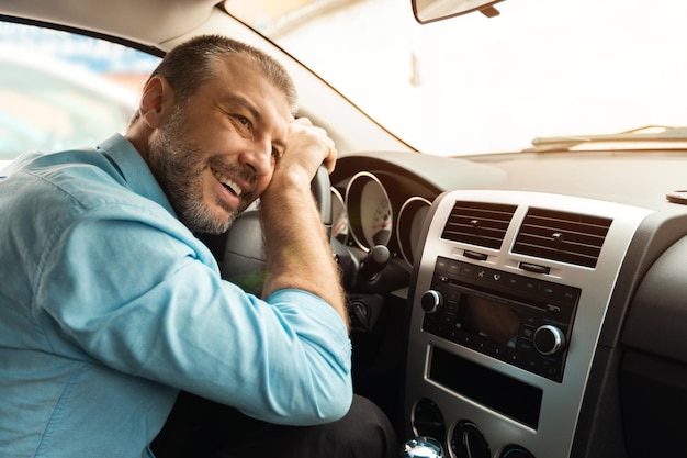 彼の新しい車の中に座っているハンドルを抱き締める幸せな男