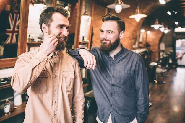 Happy guy is touching his new moustache with his hands. His friend is happy to see him like that. He is smiling to him.