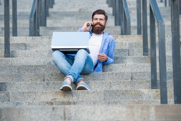 Happy guy making mobile call relaxing on stairs outdoors Smiling guyn talking on mobile phone