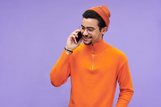 Photo happy guy in orange pullover and beanie hat talking on mobile phone