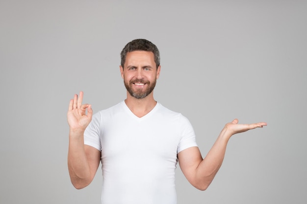 Happy guy show open hand making OK ring gesture grey background copy space presenting product