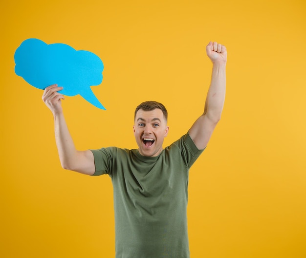 Happy guy smiling and holding blank speech balloon near head against yellow background