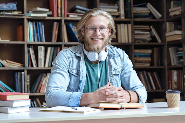 Happy guy student study in library looking at camera sit at desk