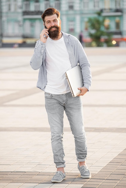 Foto ragazzo felice che parla al cellulare camminando per strada sorridente ragazzo che effettua chiamate mobili all'aperto