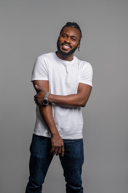 Happy guy with his wristwatch standing by the gray wall