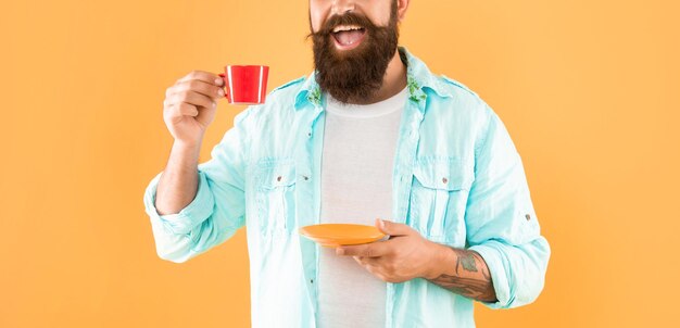 ソーサーの黄色の背景の休憩を保持しているカップからコーヒーを飲む幸せな男クロップ ビュー