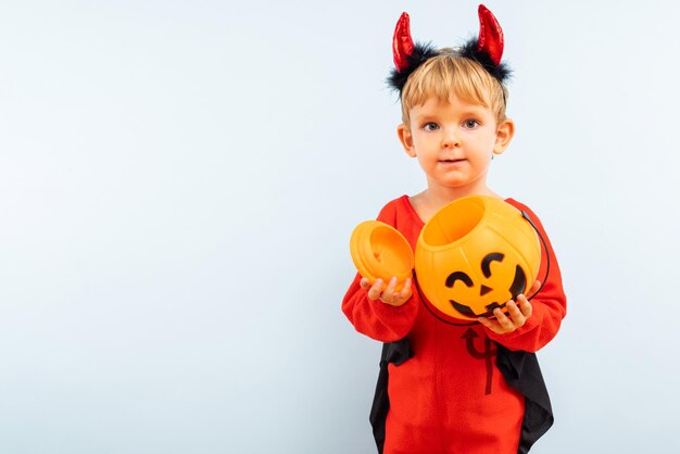 ハロウィーンの幸せな可愛い男の子 悪魔のハロウィーンコスチュームと南瓜のバスケット