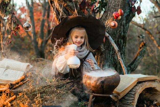 Photo happy halloween. a cute girl in a witch costume is in the witch's den. cute cheerful little witch brews a magic potion. halloween.
