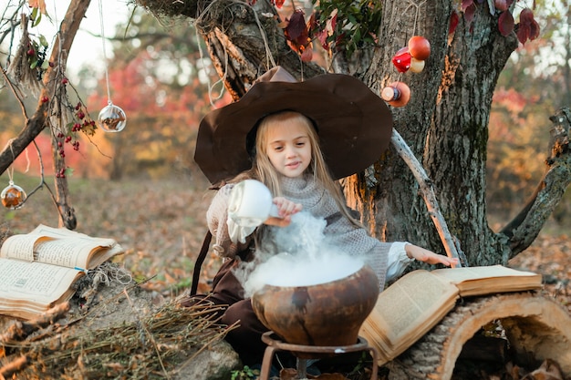 Happy Halloween. A cute girl in a witch costume is in the witch's den. Cute cheerful little witch brews a magic potion. Halloween.