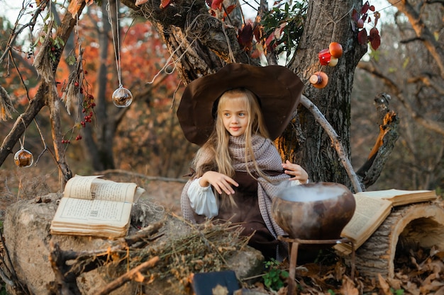 Happy Halloween. A cute girl in a witch costume is in the witch's den. Cute cheerful little witch brews a magic potion. Halloween.