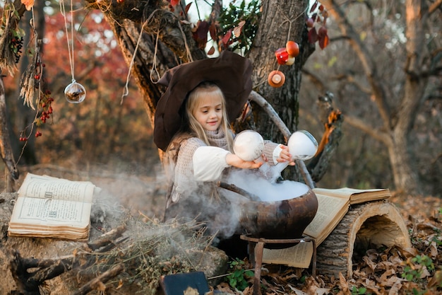 Felice halloween. una ragazza carina in costume da strega è nella tana della strega. la piccola strega allegra e carina prepara una pozione magica. halloween.