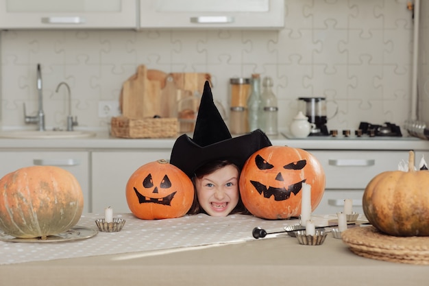 Фото Счастливого хэллоуина. милая маленькая девочка в костюме ведьмы с резьбой по тыкве. счастливая семья готовится к хэллоуину.