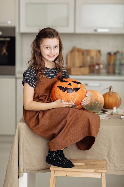 幸せなハロウィーン。カボチャの彫刻と魔女の衣装でかわいい女の子。ハロウィーンの準備をしている幸せな家族。