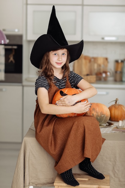 幸せなハロウィーン。カボチャの彫刻と魔女の衣装でかわいい女の子。ハロウィーンの準備をしている幸せな家族。