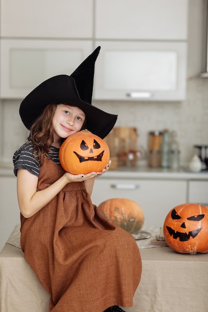 幸せなハロウィーン。カボチャの彫刻と魔女の衣装でかわいい女の子。ハロウィーンの準備をしている幸せな家族。