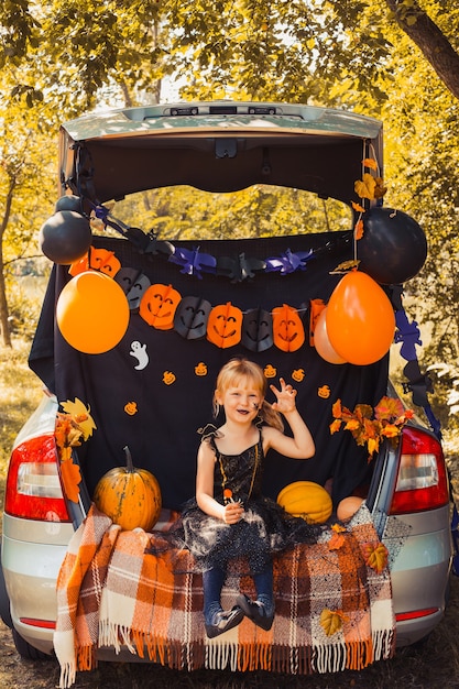 Happy halloween cute little witch with a pumpkins in trunk of car