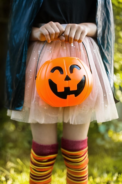 幸せなハロウィーンの日 魔女の衣装を着た小さな子供が、カボチャのジャックのバケツでキャンディーを探しています