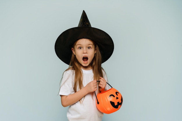 Foto happy halloween een bang meisje in een heksenhoed en met een emmer in de vorm van een pompoen zegt wow copy space advertentieruimte