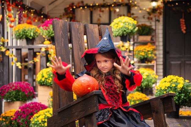 happy Halloween a girl in a witch costume with a pumpkin having fun in the fall near the house