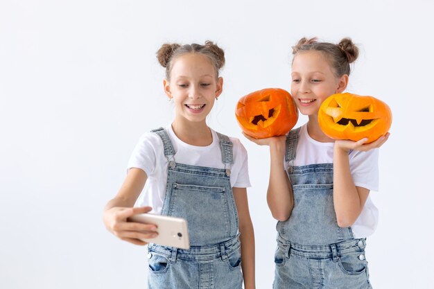 Happy Halloween, holidays and childhood concept - Cute little twins sisters girls with a pumpkins Jack-o'-lantern having fun while spending time indoors.