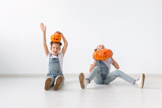 ハッピーハロウィン、休日、子供時代のコンセプト-カボチャのジャック・オー・ランタンとかわいい双子の姉妹の女の子が屋内で時間を過ごしながら楽しんでいます