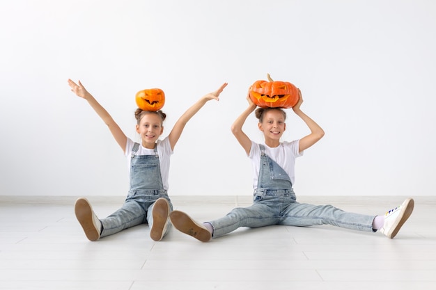 ハッピーハロウィン、休日、子供時代のコンセプト-カボチャのジャック・オー・ランタンとかわいい双子の姉妹の女の子が屋内で時間を過ごしながら楽しんでいます