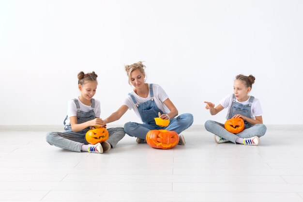 Happy halloween and holidays concept - A mother and her daughters with pumpkins. Happy family preparing for Halloween.