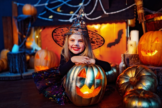 Happy Halloween. A little beautiful girl in a witch costume celebrates with pumpkins