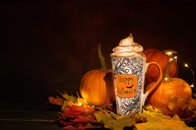 Photo happy halloween mug with whispered cream in front of orange pumpkins on dark background.