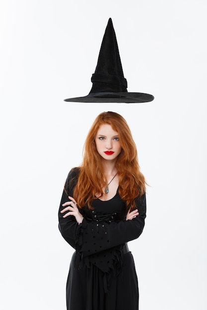 Photo happy halloween sexy ginger hair witch with magic hat flying over her head