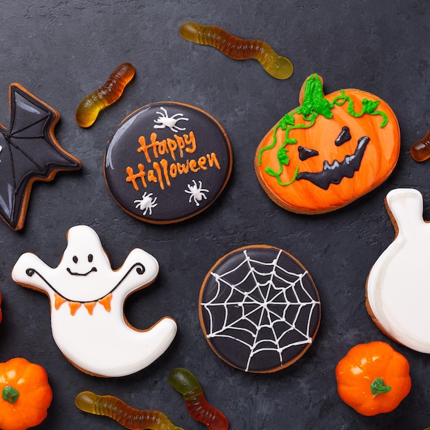 Happy halloween sweets for party gingerbread cookies and gummy worms on a dark table