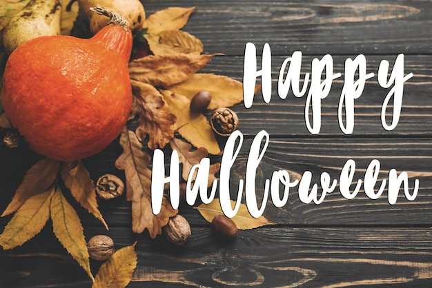 Happy Halloween Text on Beautiful Pumpkin with bright autumn leaves acorns nuts on wooden rustic table flat lay Atmospheric image Seasons greeting card