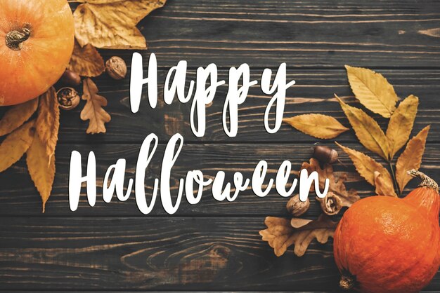 Happy Halloween Text on Beautiful Pumpkin with bright autumn leaves acorns nuts on wooden rustic table flat lay Atmospheric image Seasons greeting card