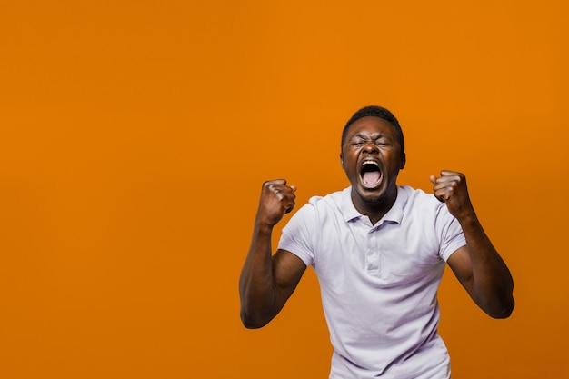 Happy handsome black man wins online bet on orange surface